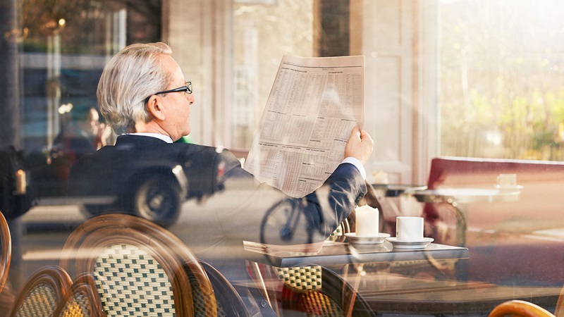 Older business man reading financial newspaper in cafe