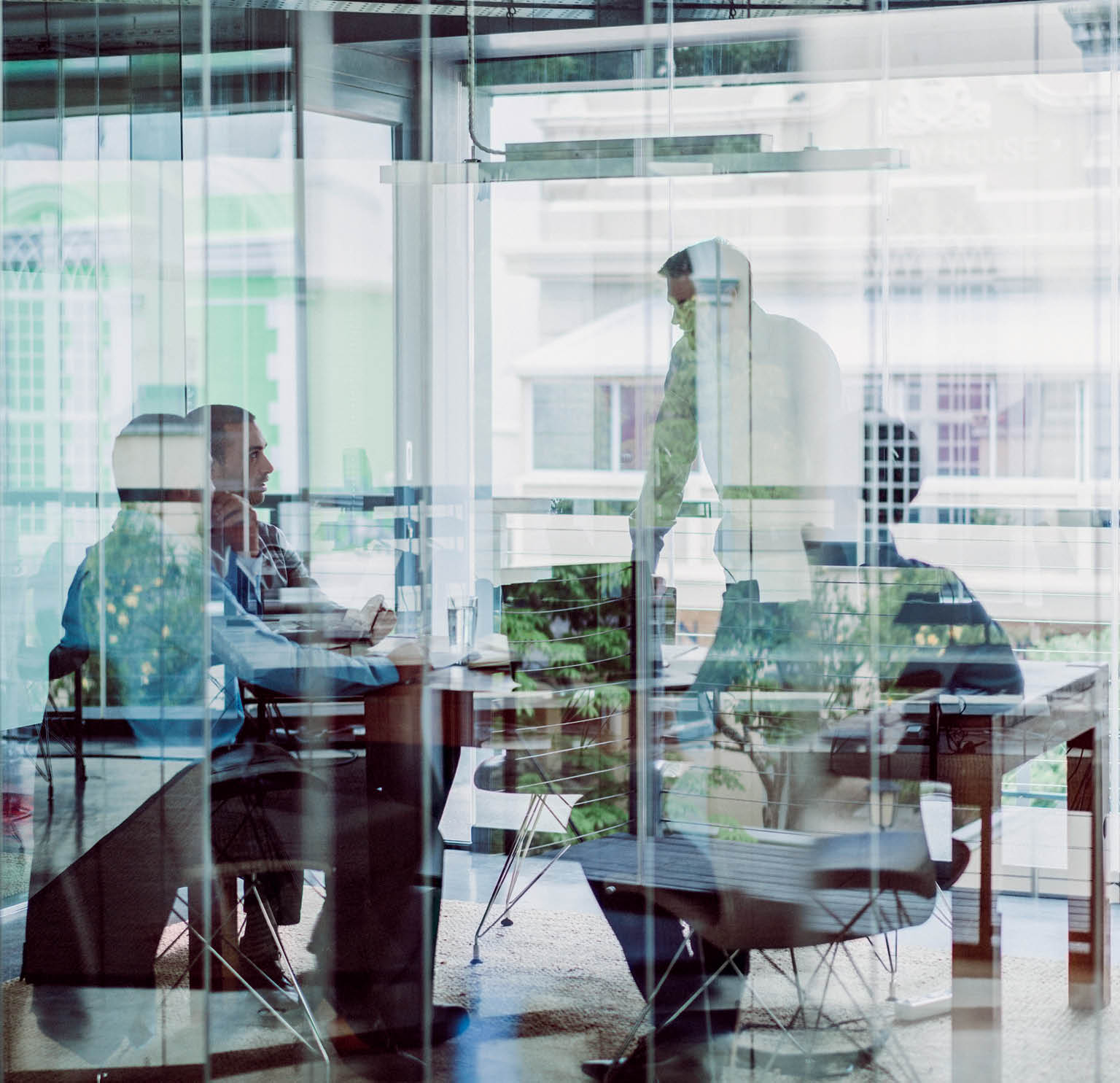 Business colleagues in meeting at office  Male and female professionals are planning strategy in brightly lit workplace  They are seen through glass wall with reflections 